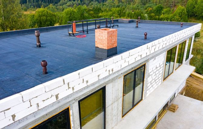 Flat roof of a modern building with a brick chimney and several vents.
