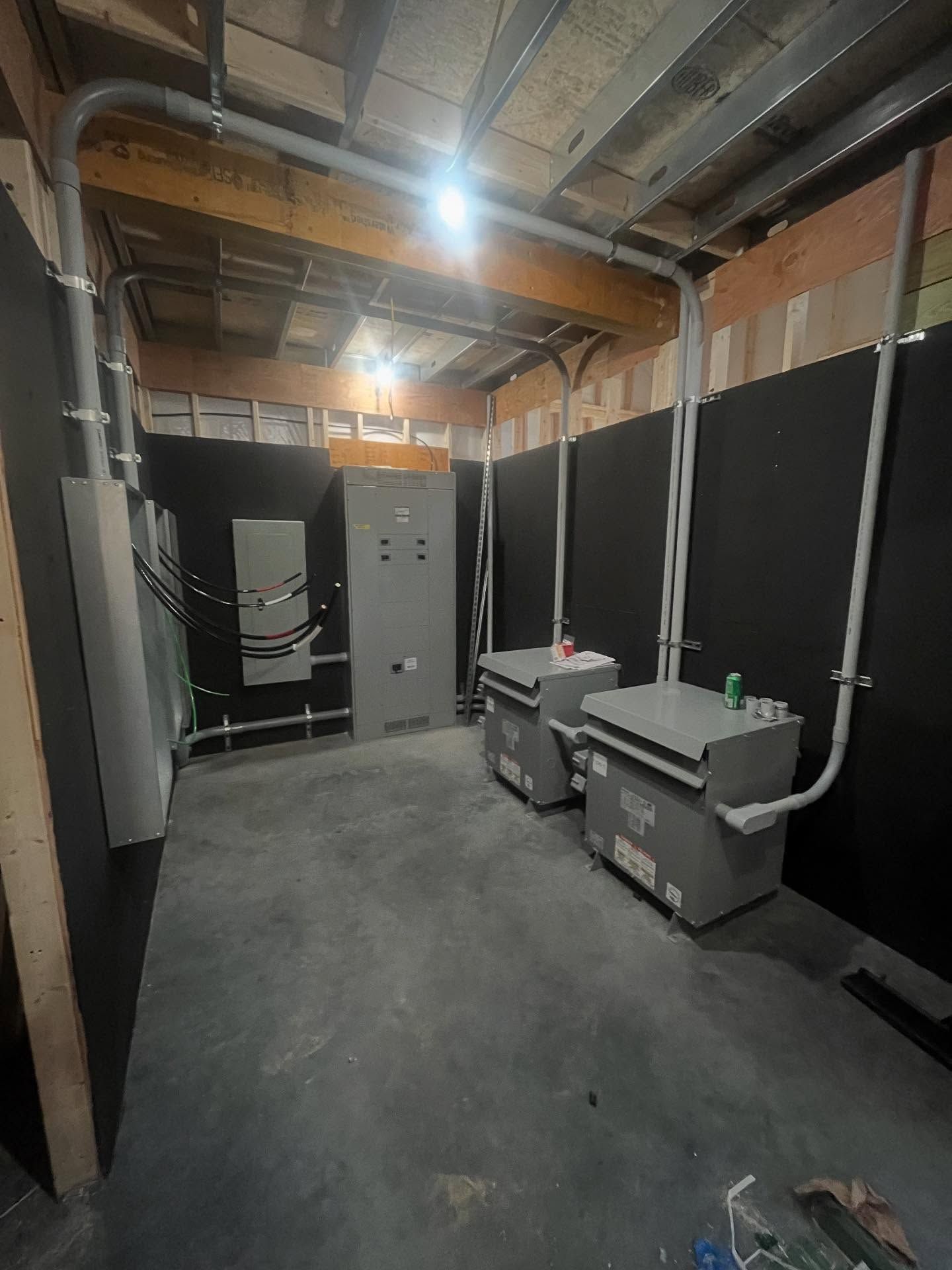 Electrical equipment in a room, with metal conduit, breakers, and two grey boxes. Black wall backdrop.