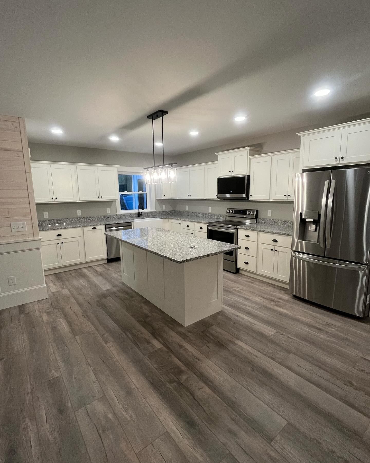 Modern kitchen with white cabinets, granite countertops, stainless steel appliances, and a central island.
