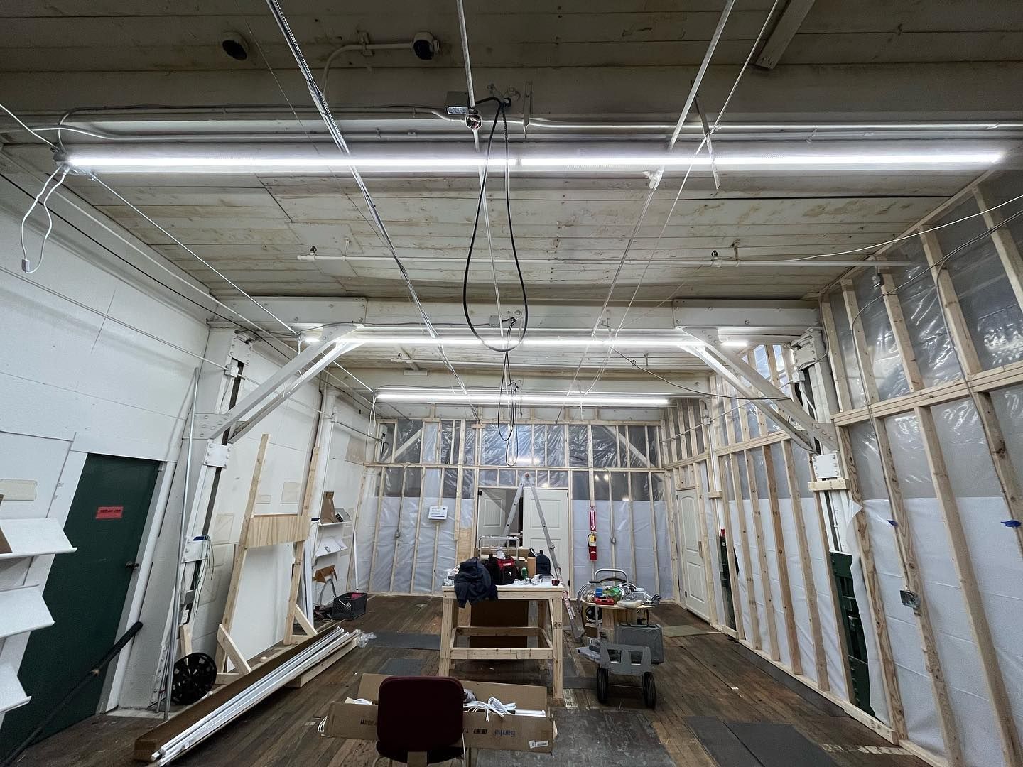 Interior workshop under construction with wooden beams, fluorescent lights, and scattered tools.
