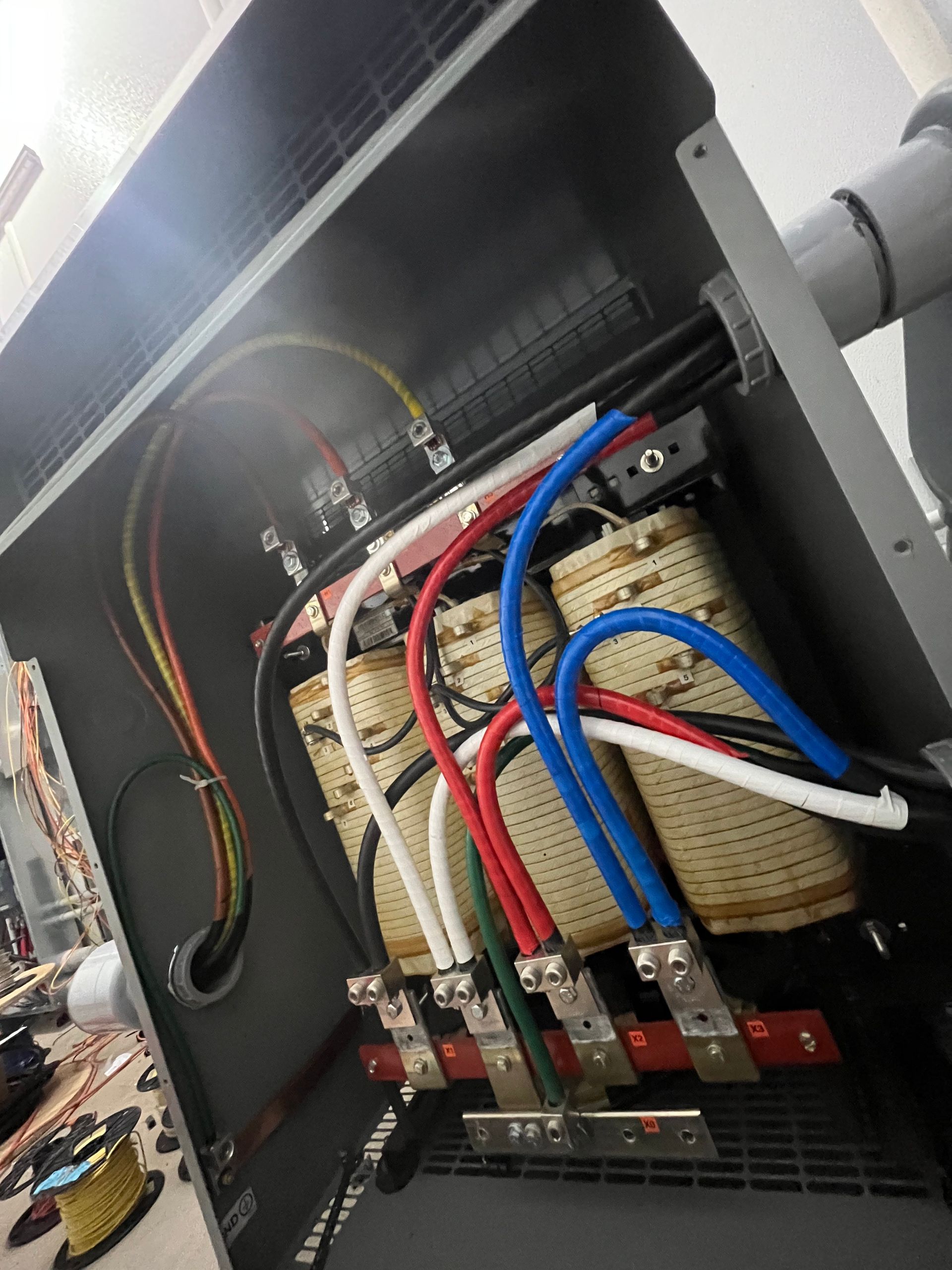 Electrical transformer inside a gray metal cabinet, with various colored wires connected to terminals.