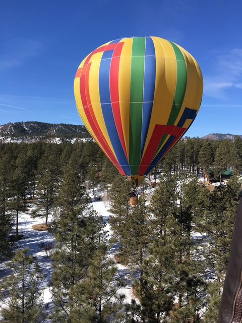 A colorful hot air balloon is flying over a snowy forest