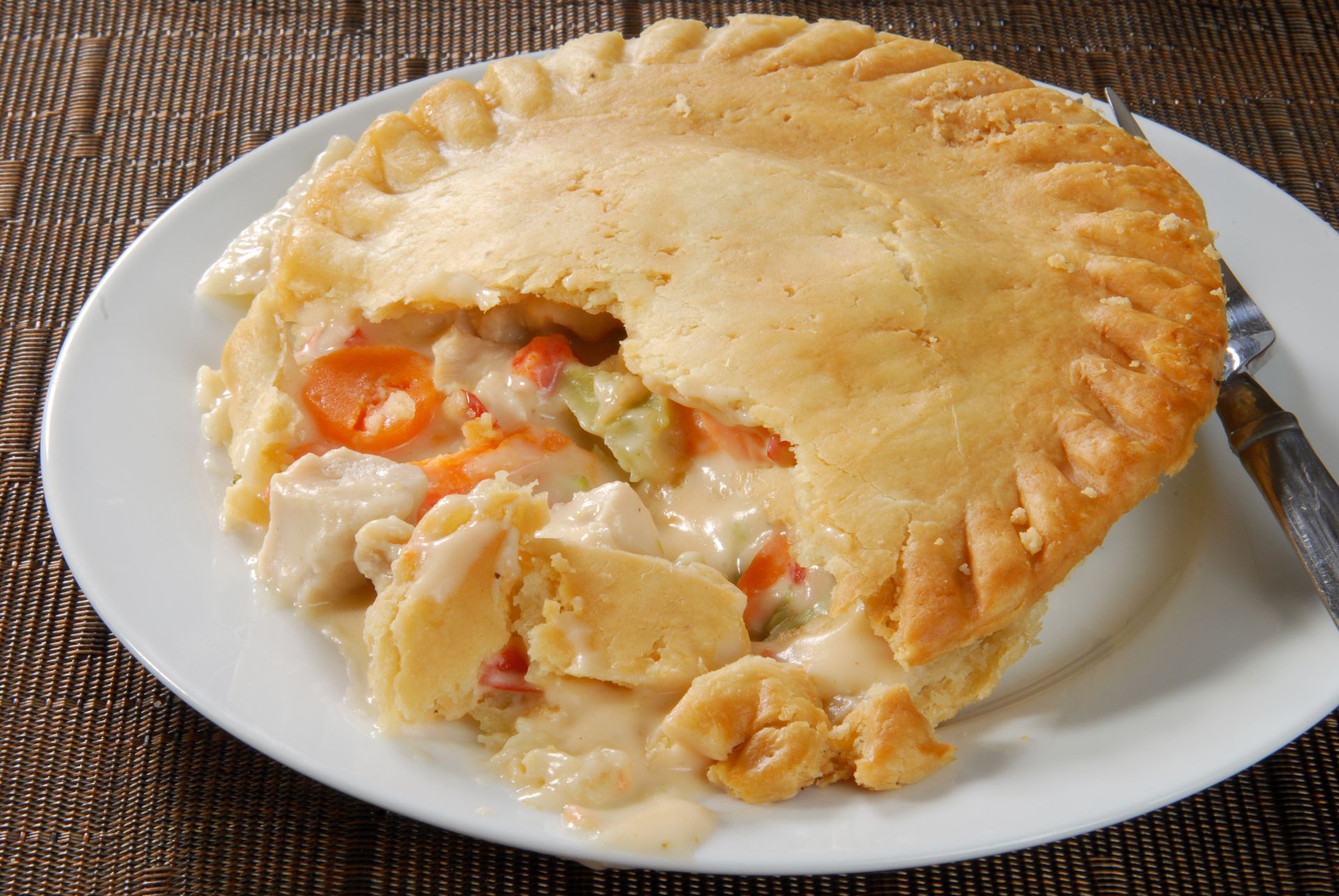 A white plate topped with a chicken pot pie with a slice taken out of it.