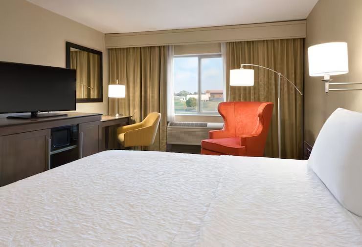 A hotel room with a bed , chair , desk and television