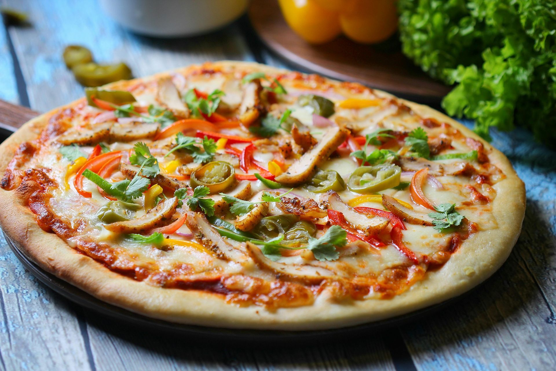A pizza with chicken , peppers , and cheese on a wooden table.