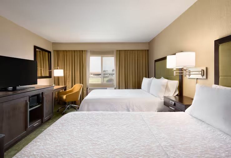 A hotel room with two beds , a desk , a television and a window.