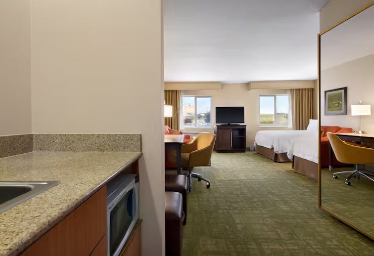 A hotel room with a king size bed , desk , chairs and a microwave.