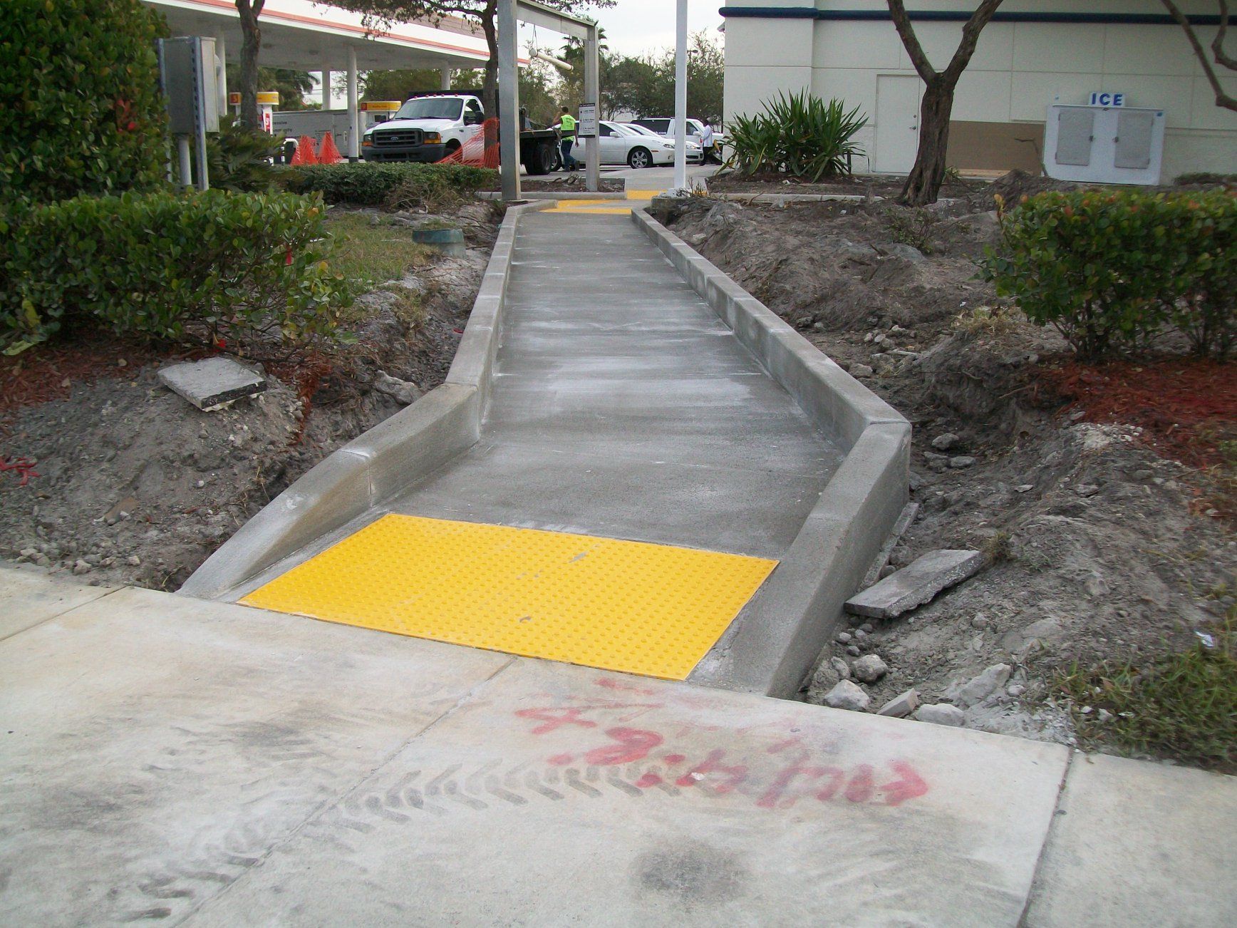 Concrete sidewalk with yellow tactile paving leading to a gas station.