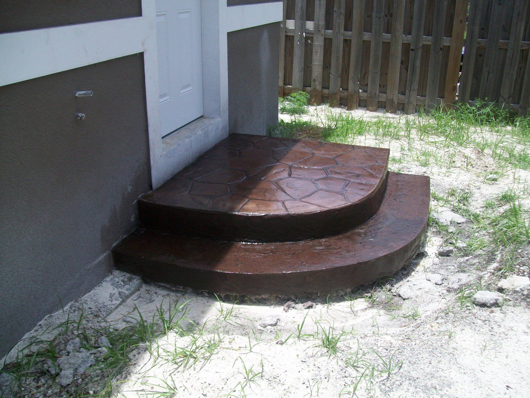 Brown, two-step concrete stoop leading to a white door; next to a brown building.