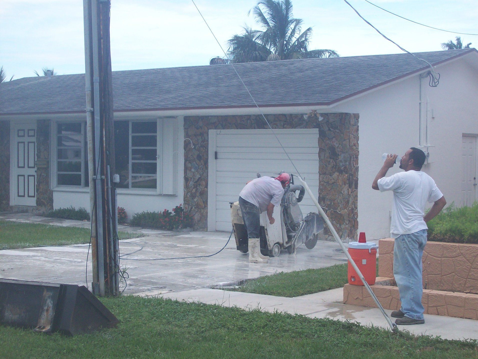Two people pressure washing a scooter in front of a house. One person drinks from a bottle.