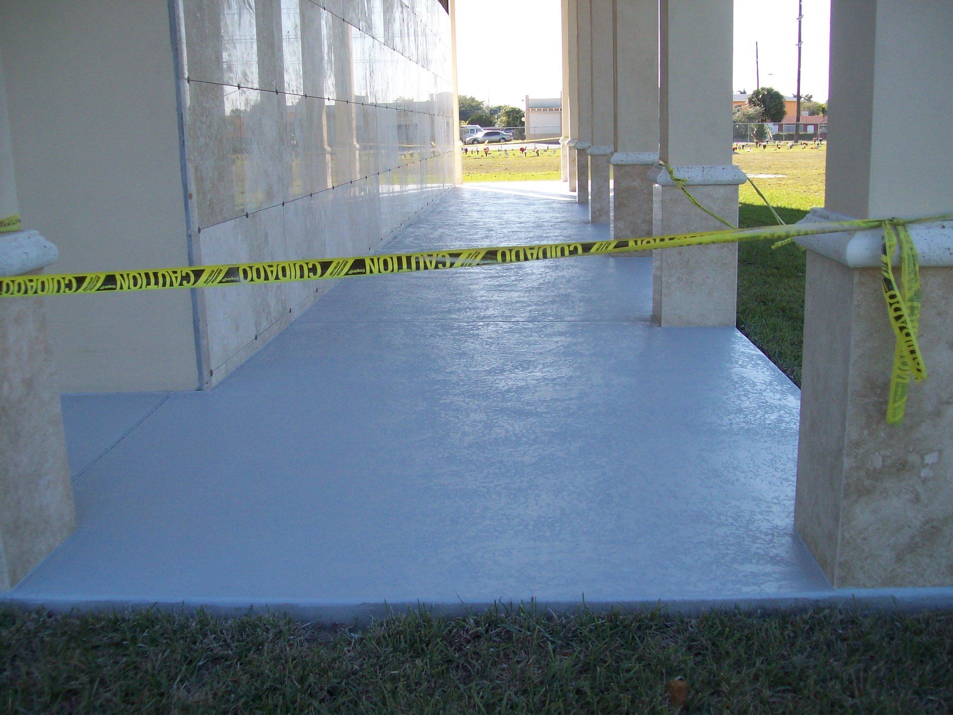 A covered outdoor area with a freshly painted gray floor, caution tape, and columns.