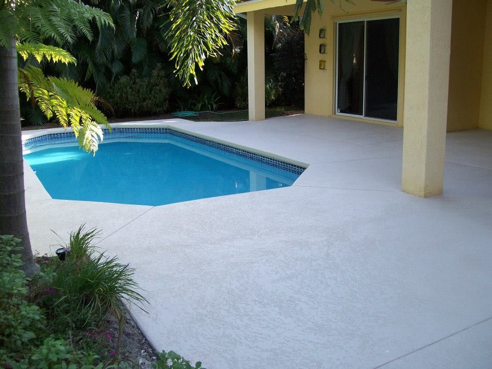 Pool area with light gray concrete patio, turquoise pool, and cream-colored house.