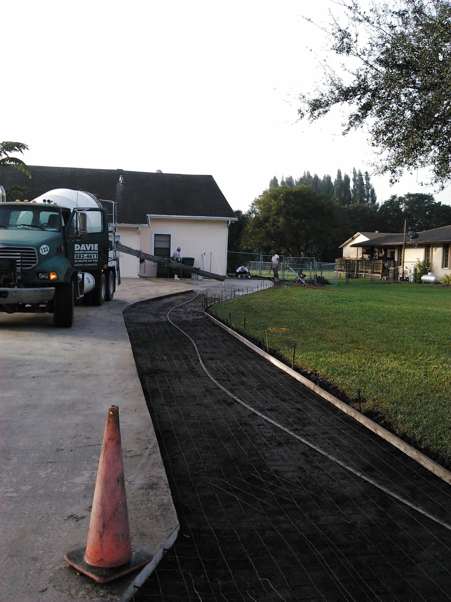 Cement truck pouring concrete for a driveway next to a grass lawn; orange traffic cone in foreground.
