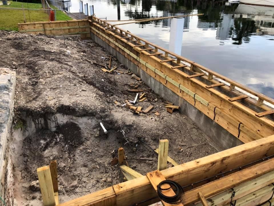 Yellow excavator loading dirt into a red dump truck on a dirt hill under a blue sky.