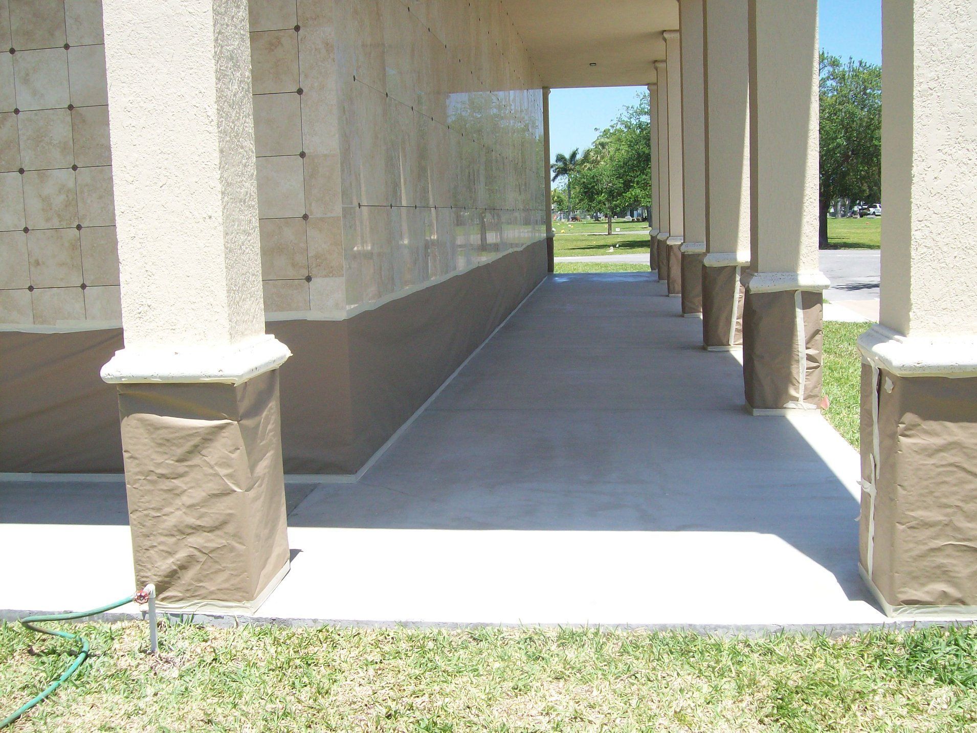 Covered walkway with columns and a beige stone wall at a cemetery.