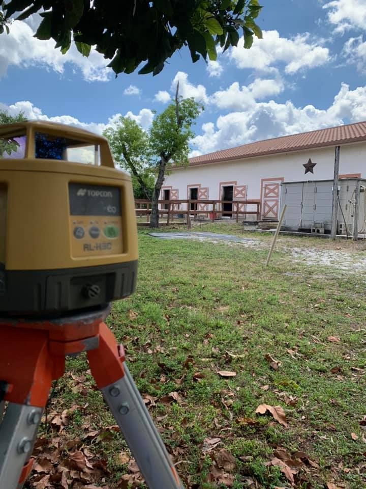 A yellow laser level on a tripod in a grassy area, aimed at a white building with a star, under a blue sky.