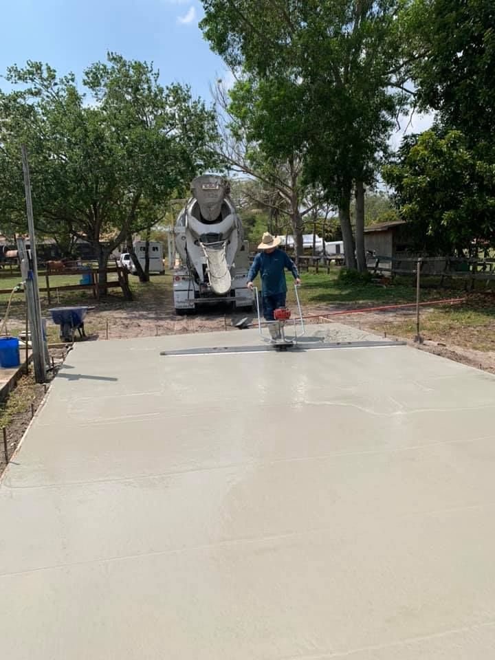 Concrete pour: A worker floats fresh concrete, with a mixer truck in the background, outdoors on a sunny day.