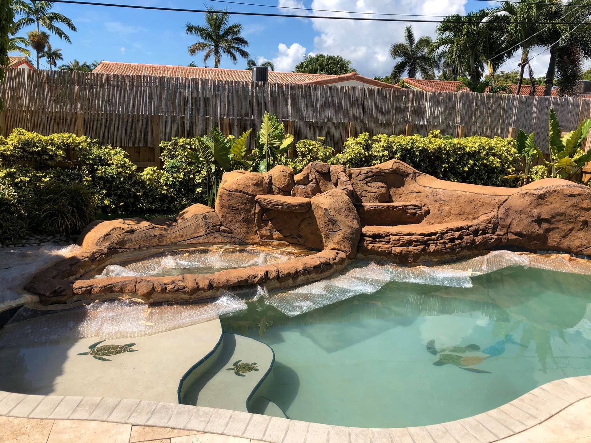 A backyard pool with a rock waterfall feature and alligator mosaic tiles.