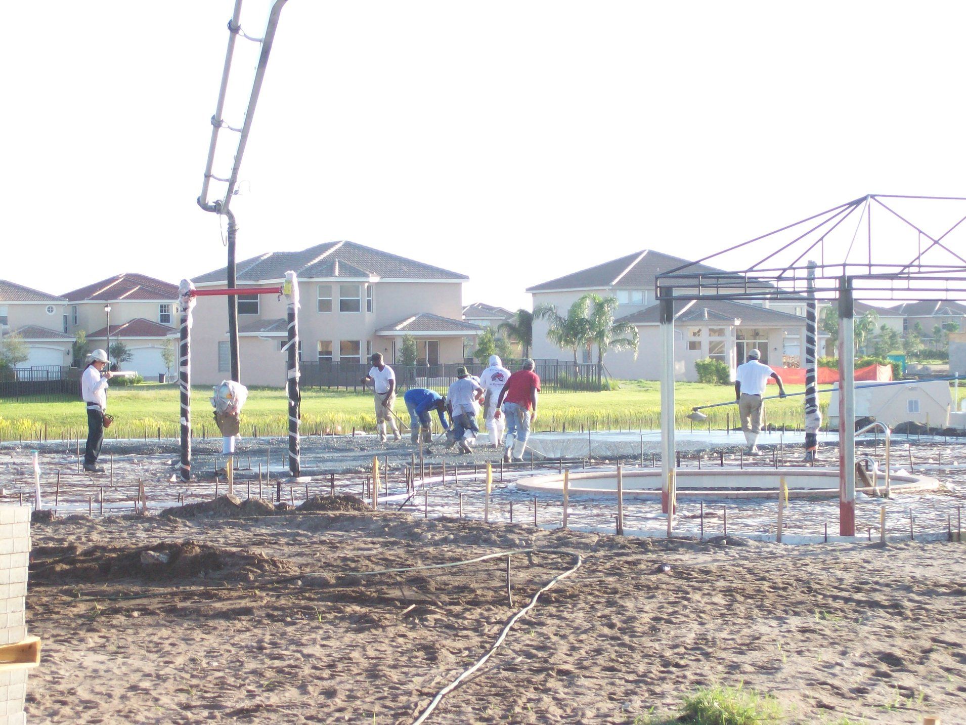 Construction workers pouring concrete at a building site, with residential houses in the background.