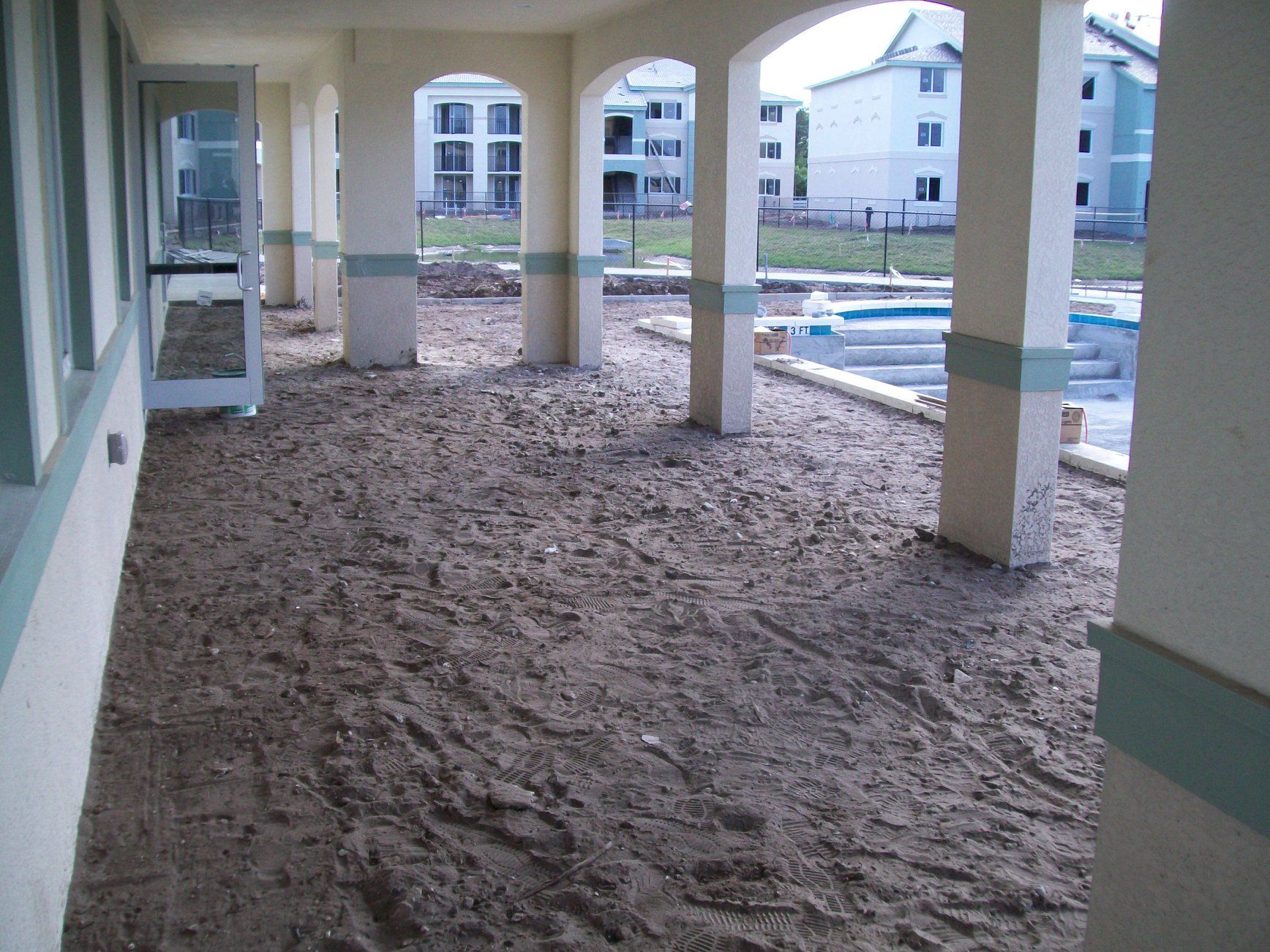 Yellow skid steer leveling gravel in a construction site with wooden posts.