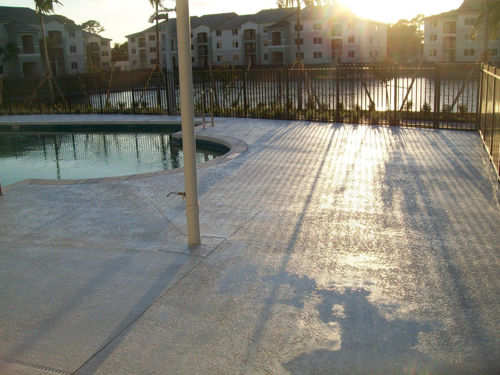 Poolside deck with textured surface, reflecting sunlight over water and buildings in the background.
