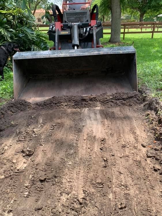 Excavator dumping dark brown mulch against a blue sky.