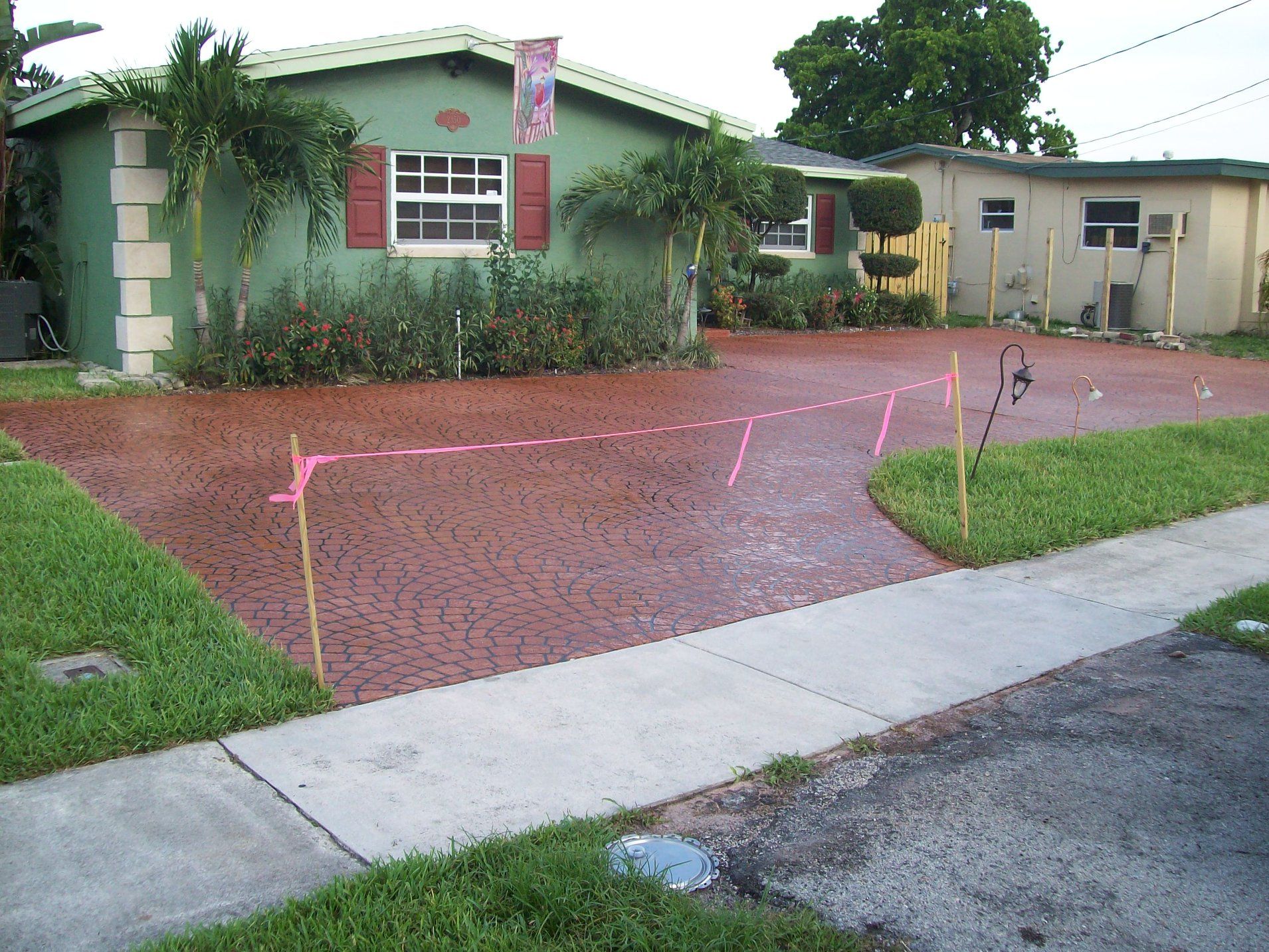 Brick driveway in front of a green house, with pink lines marking a pathway.