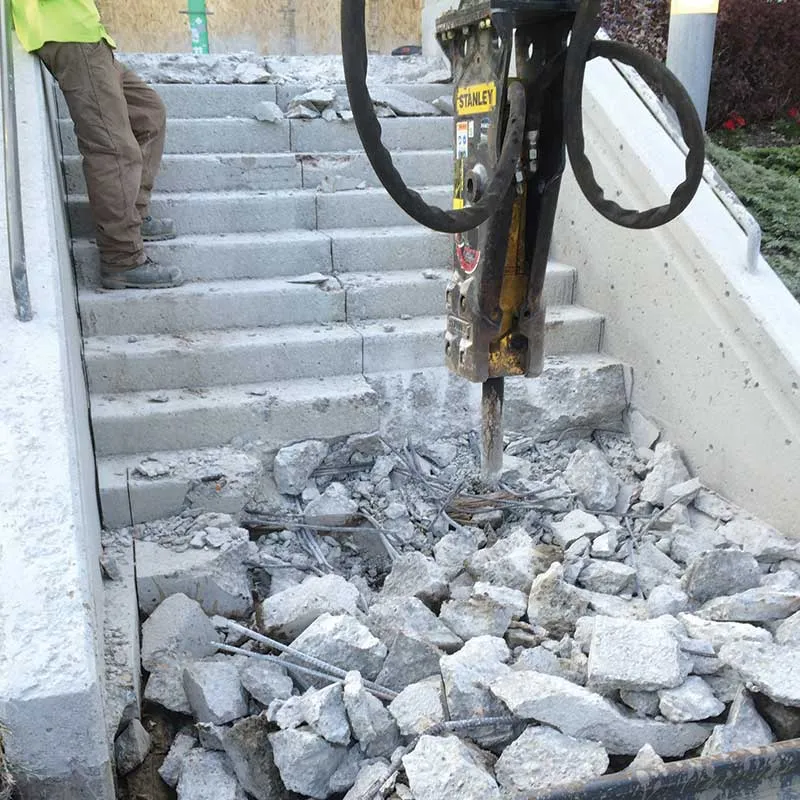 A person using a sledgehammer to break through a white wall, debris flying outwards.