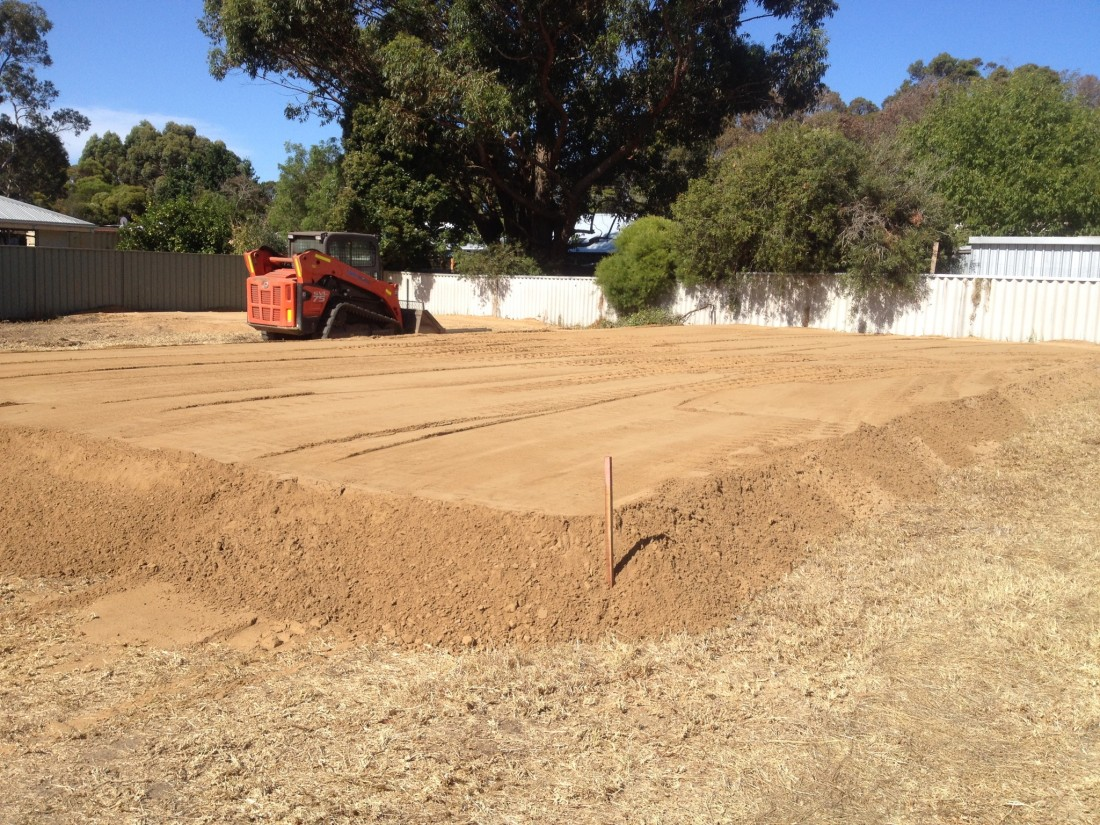 Excavator dumping dark brown mulch against a blue sky.