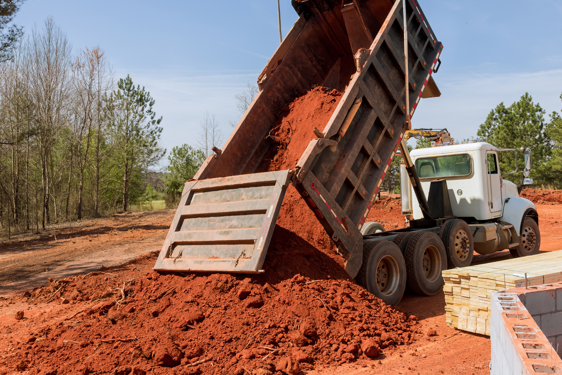 Dump truck unloading red soil on a construction site.