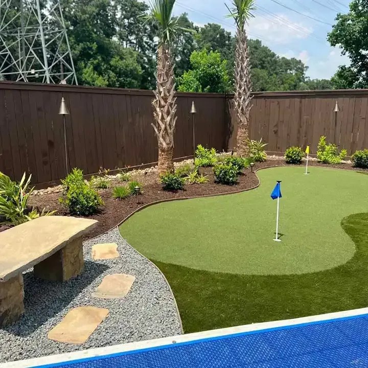 There is a putting green in the backyard next to a pool.