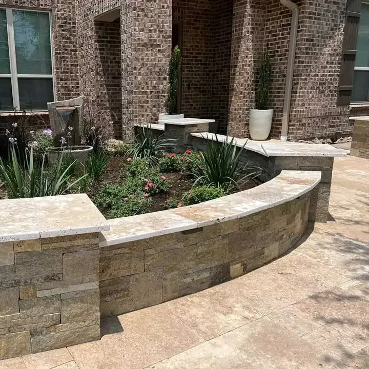 A brick house with a stone wall and a planter with flowers in front of it.