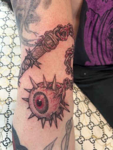 A tattoo artist sketching a custom design in a warm, art-filled studio with ink tools and framed artwork.