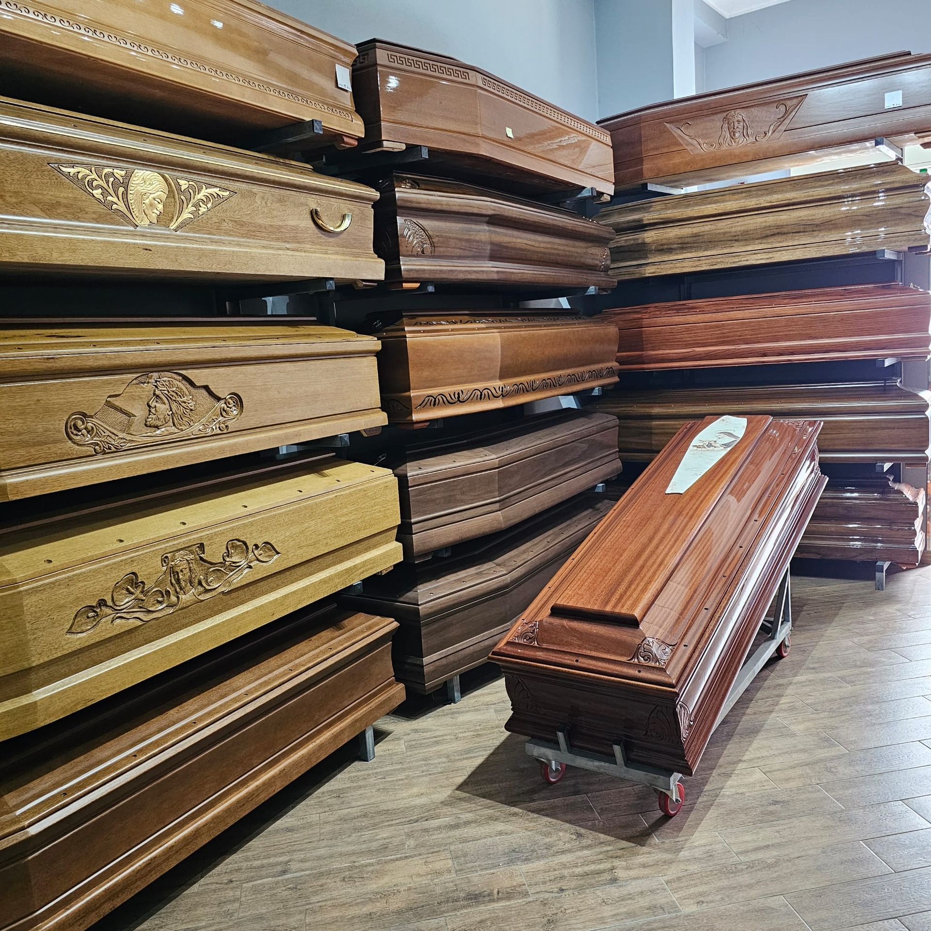 Bare di legno accatastate in un'agenzia di pompe funebri, di diverse tonalità di marrone. Una bara è su ruote.