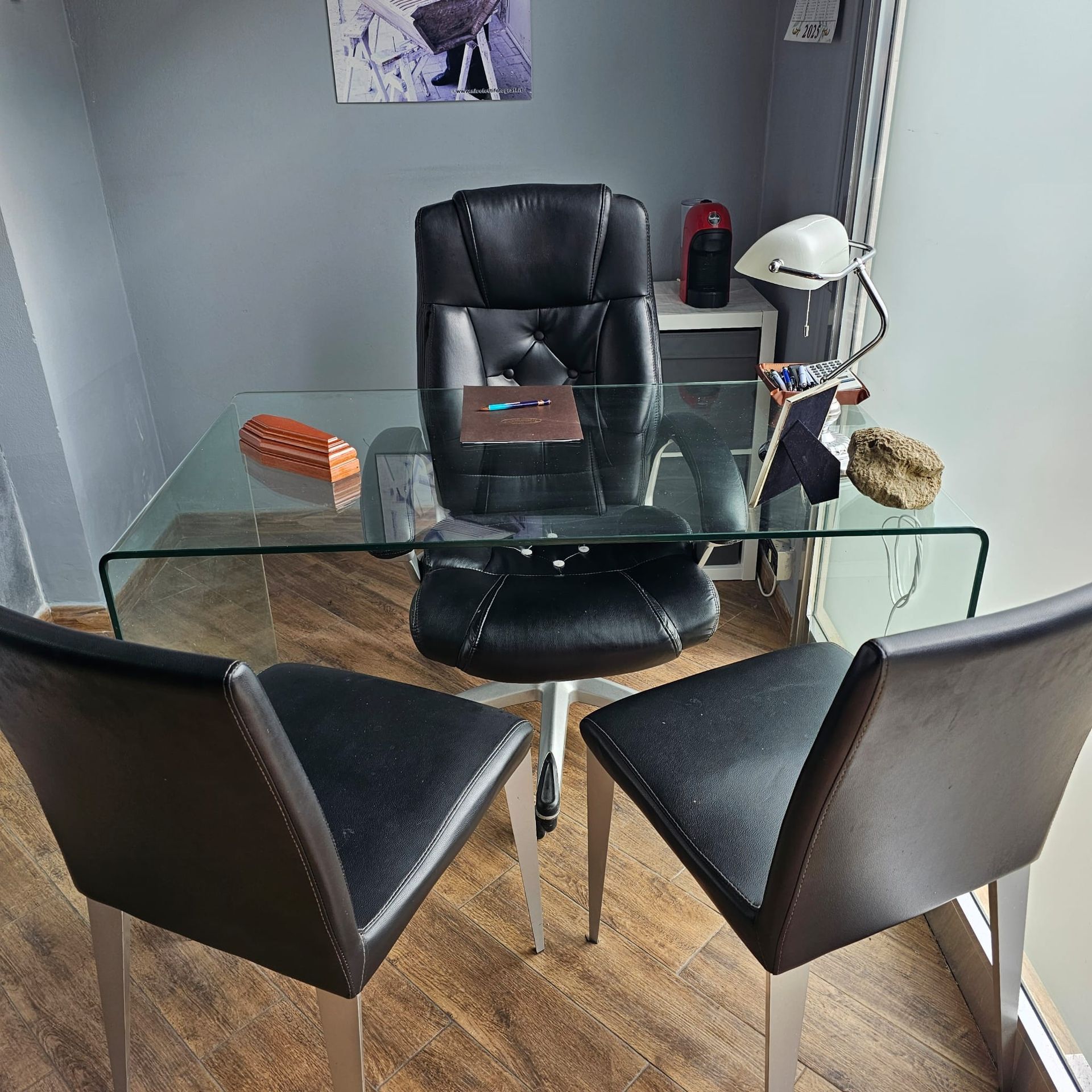 Uomo seduto a una scrivania in un piccolo ufficio con piante e piano in vetro.