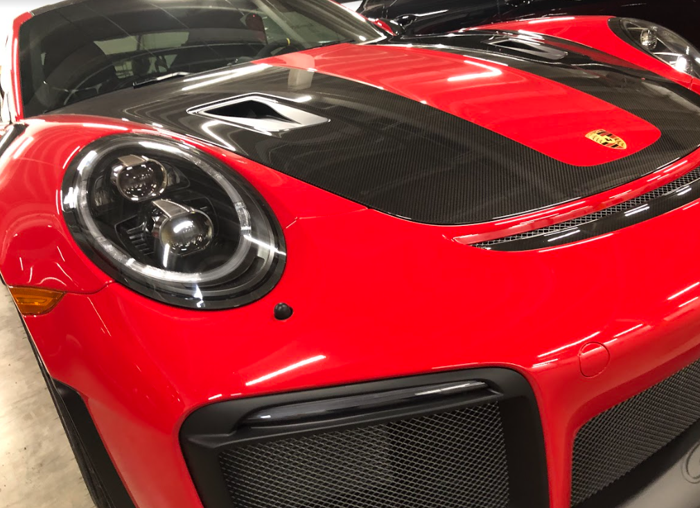 A red Porsche with a carbon fiber hood and racing stripe parked indoors.