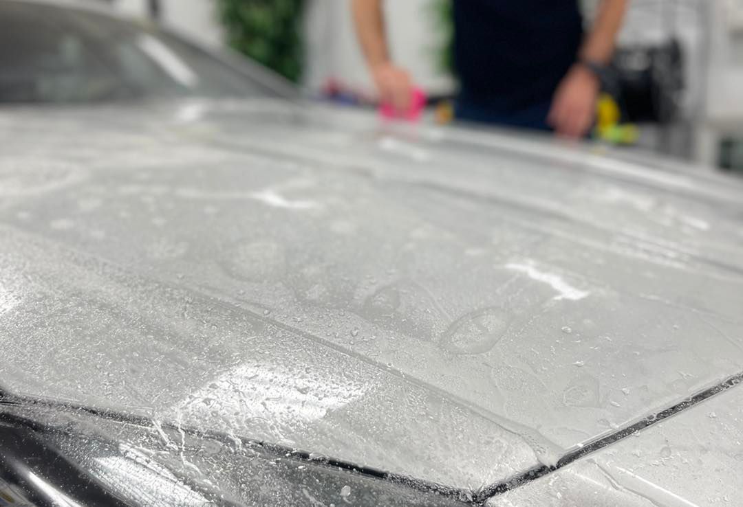 A person using a cloth to buff a soapy, wet car hood in a workshop.