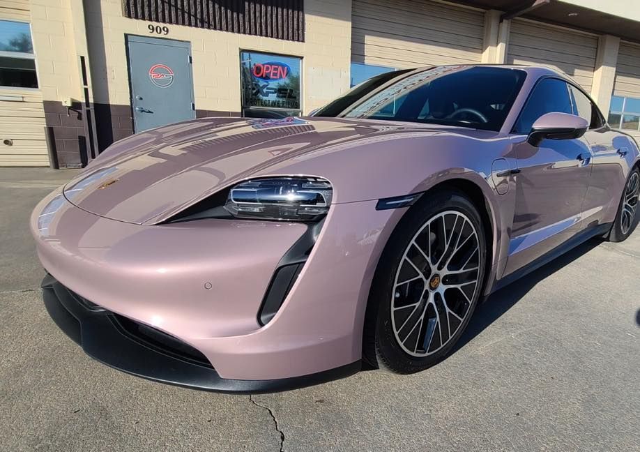 A light purple Porsche Taycan electric sedan parked in front of a commercial building.