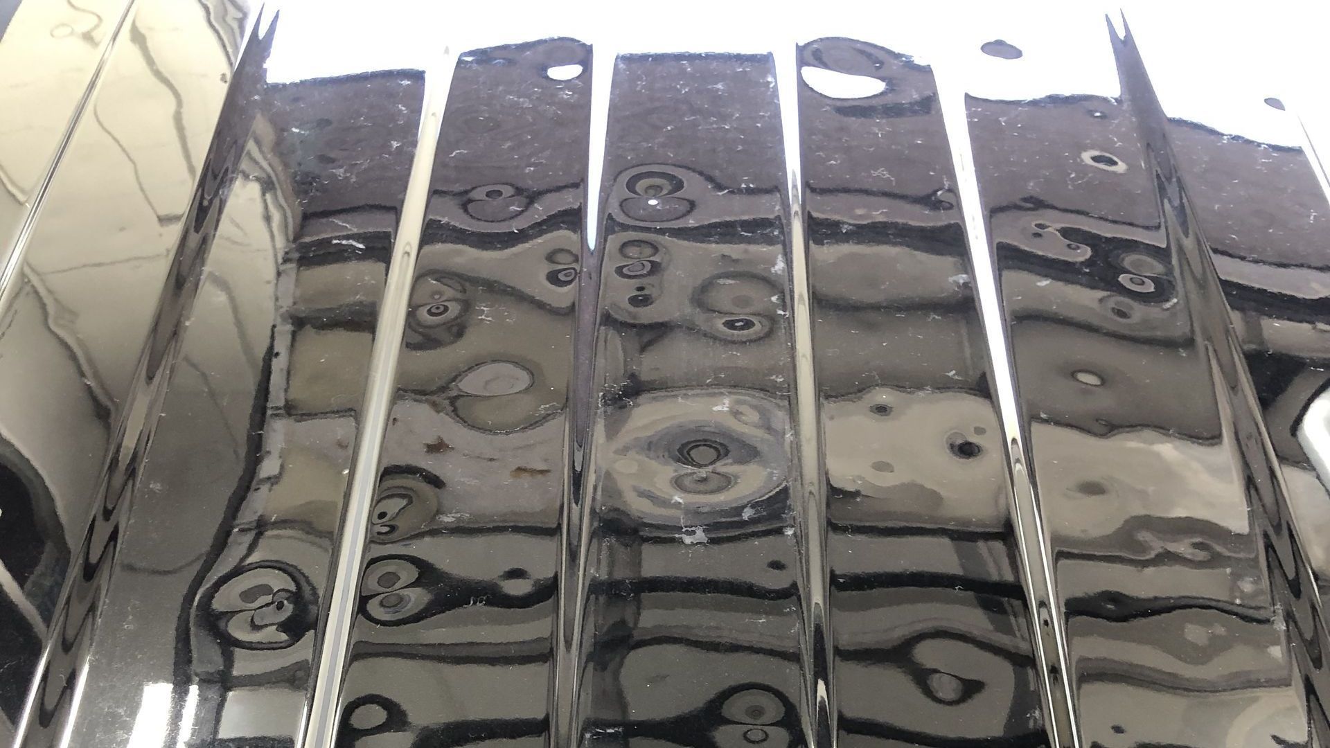 Close-up of a glossy black car door panel reflecting fluorescent workshop lights and ceiling structure.
