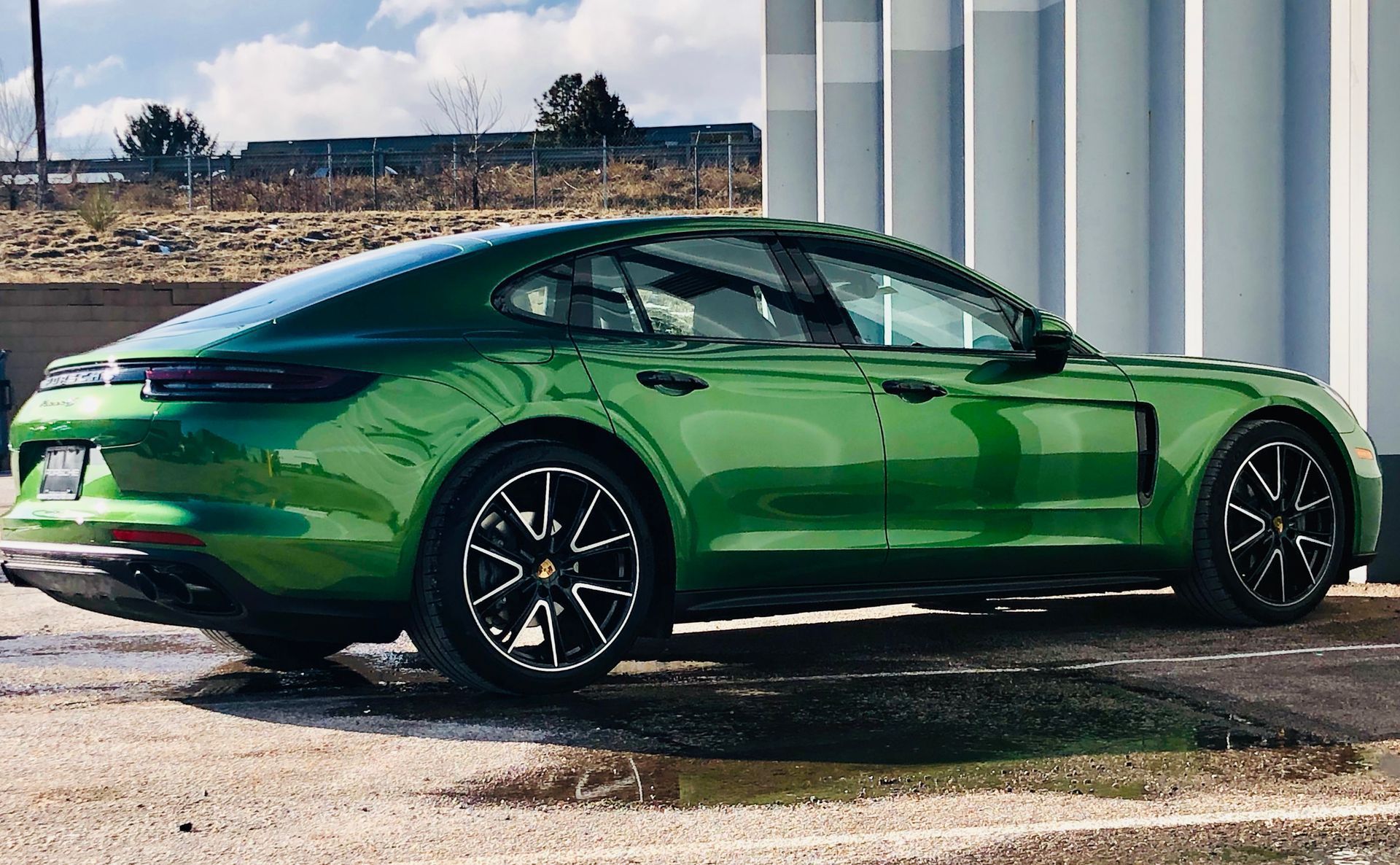 A bright green Porsche Panamera parked outdoors on a paved surface next to a white ribbed building.