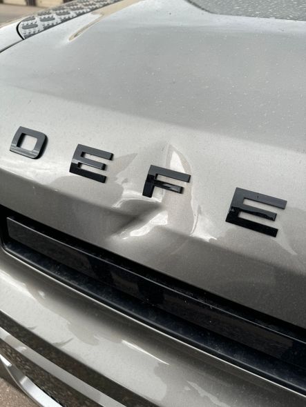 A close-up of a deep dent and paint damage on a black car fender near the orange side marker light.