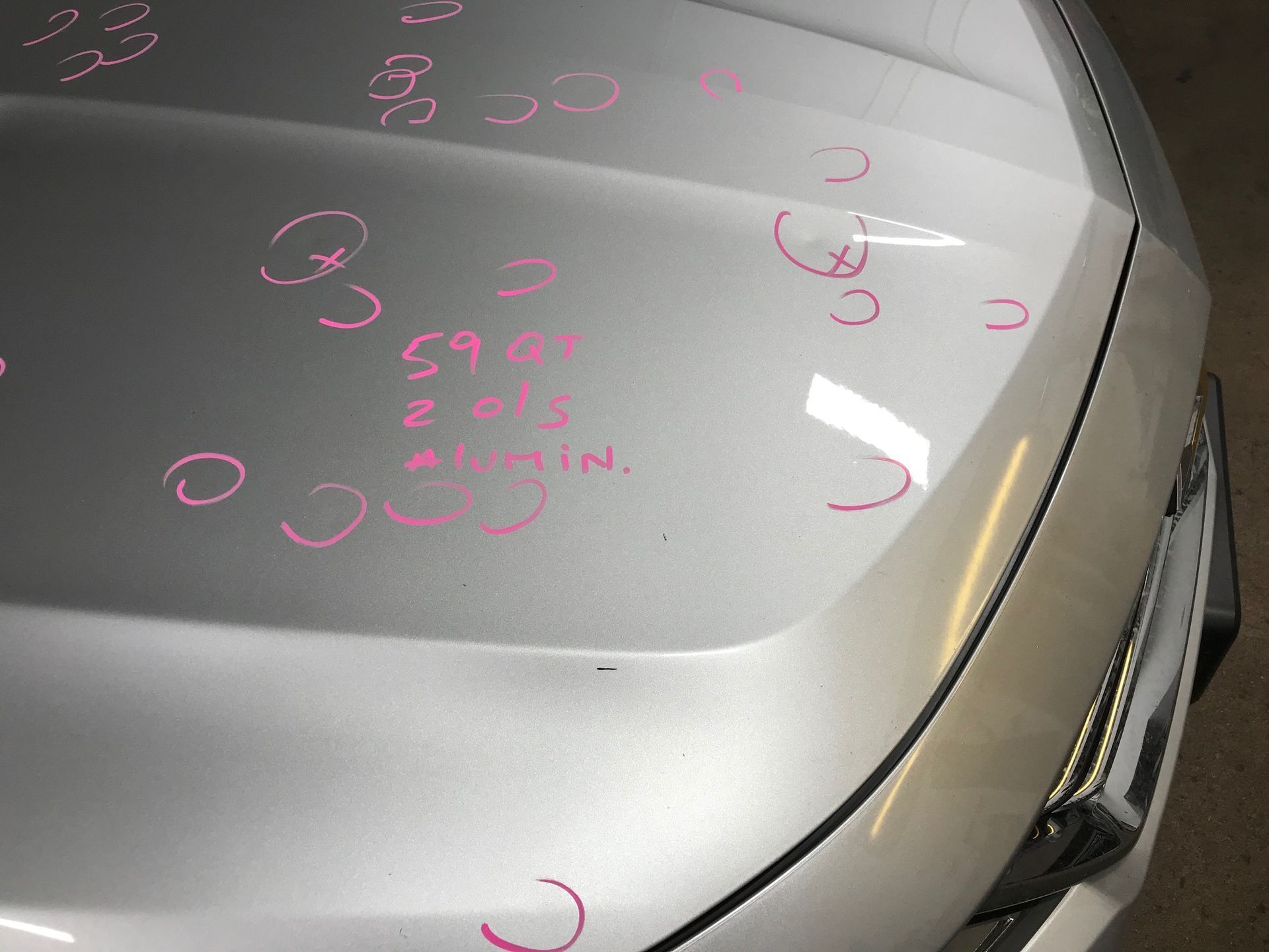A silver car hood covered in small circular pink markings highlighting hail damage.