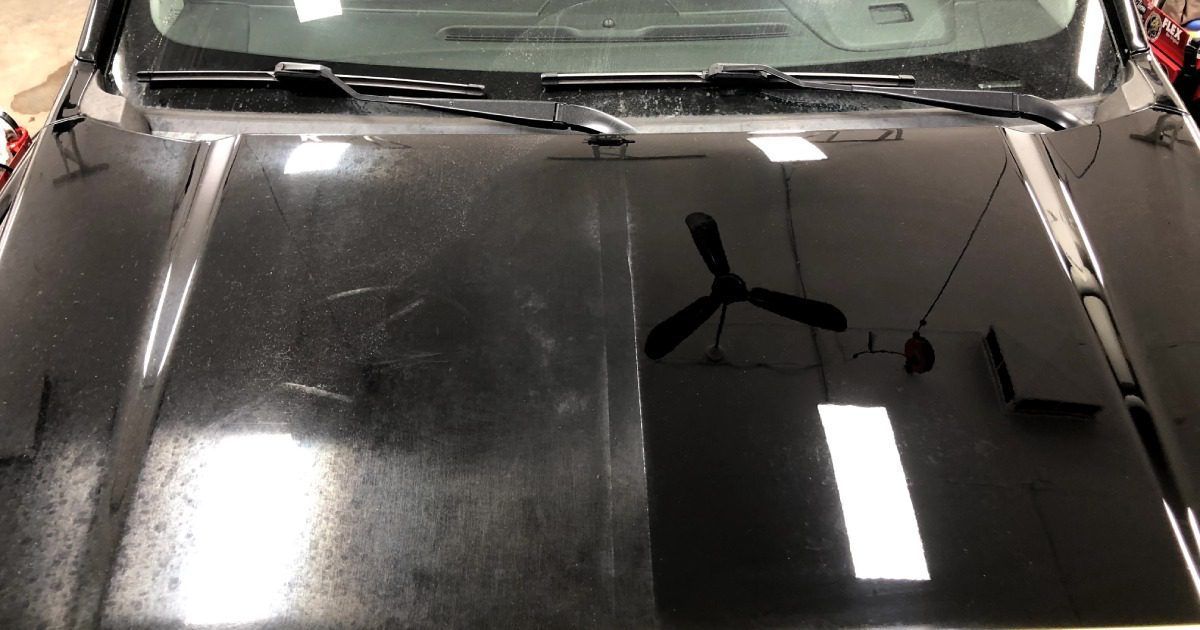A black car hood split down the middle, showing a hazy, scratched left side and a polished, reflective right side.