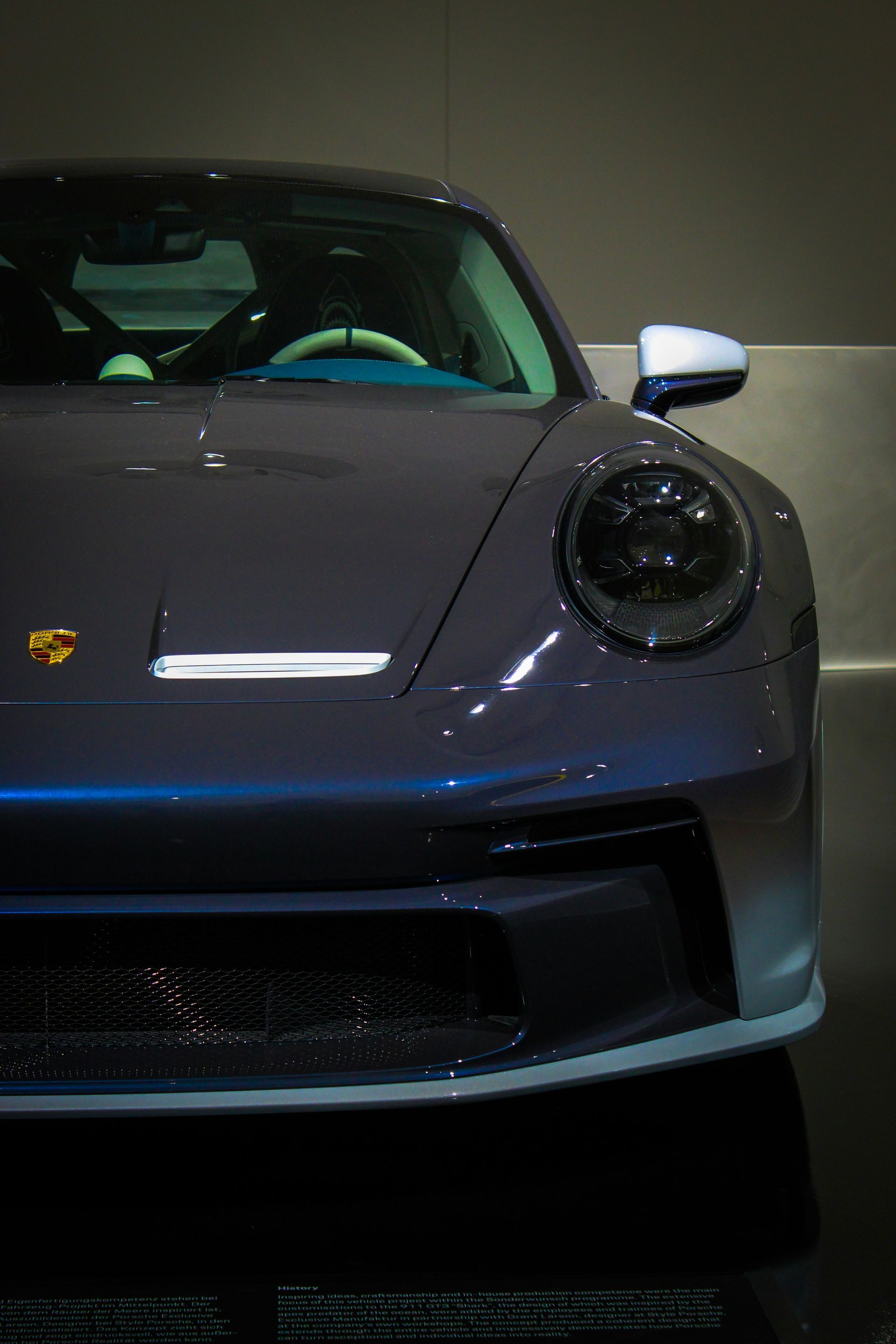Close-up of a sleek, dark grey Porsche 911 GT3 parked indoors, showcasing its iconic headlight and hood design.