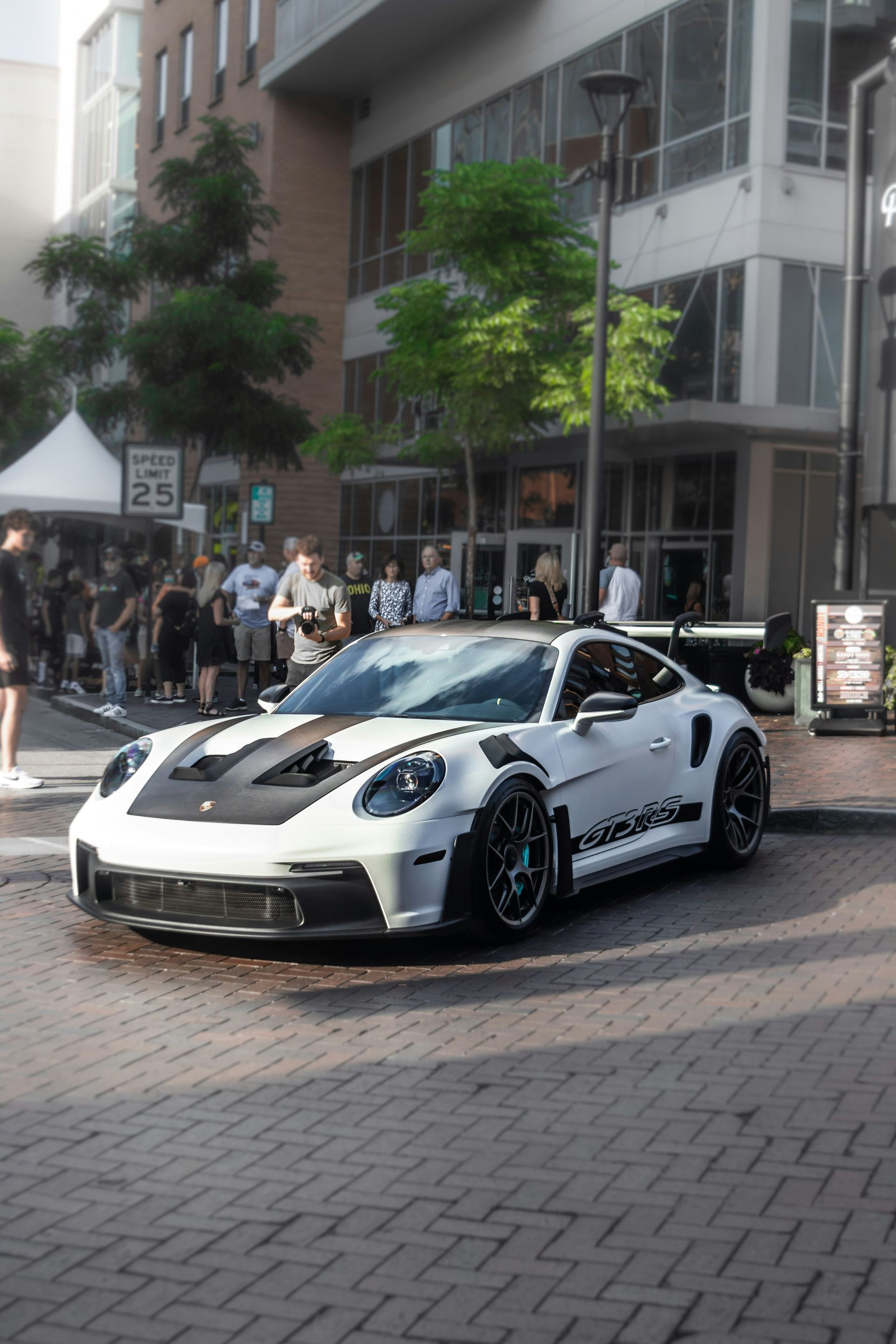 A white and black Porsche 911 GT3 RS parked on a brick street with a crowd of people in the background.