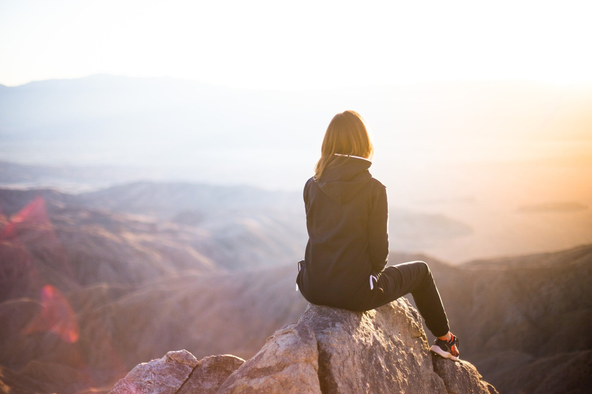 women sitting on mountain with back towards viewer - she is looking out over hazy river or valley