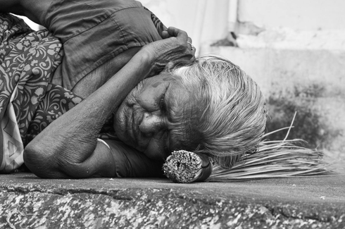 An old woman lying on the ground with her head on a woven pillow waiting for death
