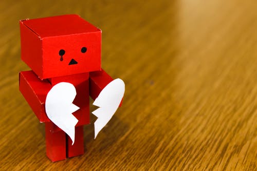 red tiny robot holding two halves broken heart
