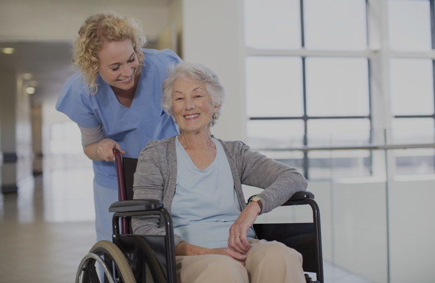 Nurse and aging patient smiling in hospital corridor
