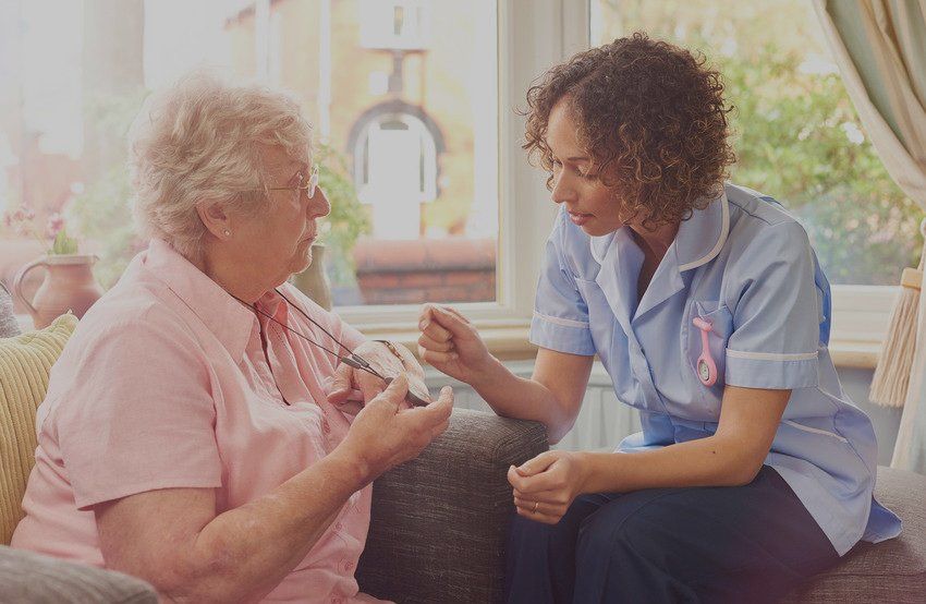 a care nurse demonstrates to a senior woman how her panic pendant would work in the event of a fall or medical emergency.